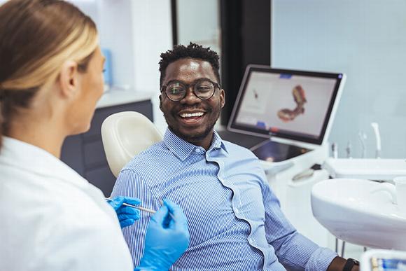 man sitting in dentist chair smiling while dental nurse talks