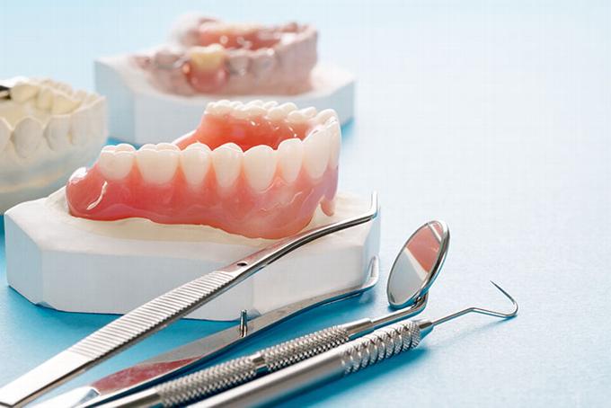 Partial and complete dentures sitting next to dentist tools